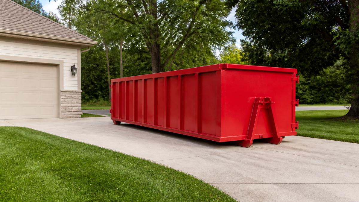 Roll-off dumpster positioned on residential driveway with clear space around it and no overhead obstacles visible